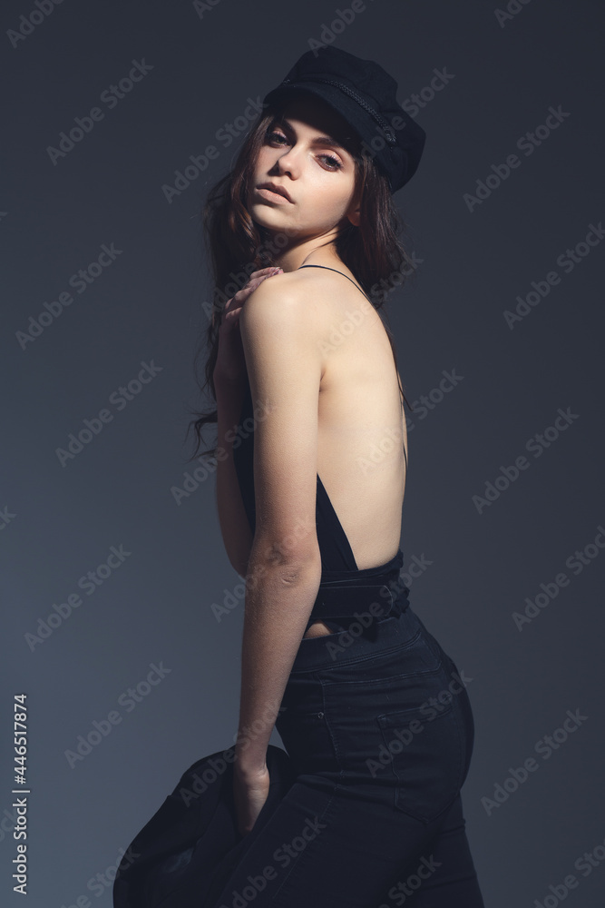 Fashionable girl portrait with hard studio light. Sexy model in a hat on a gray background. Fashionable girl portrait with hard studio light. Sexy model in a hat on a gray background.