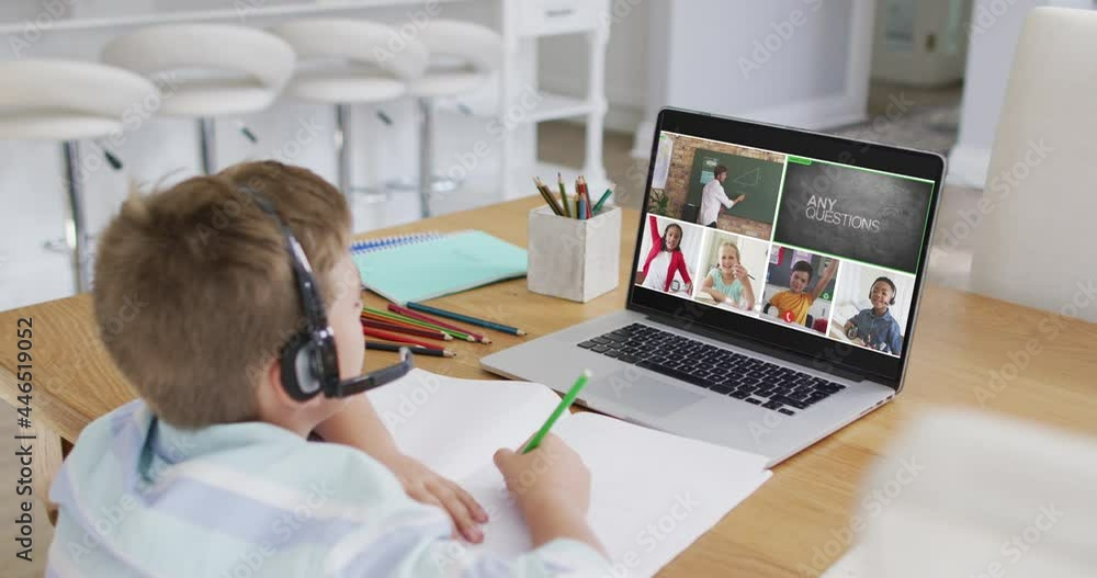 Schoolboy using laptop for online lesson at home, with diverse teacher and class on screen