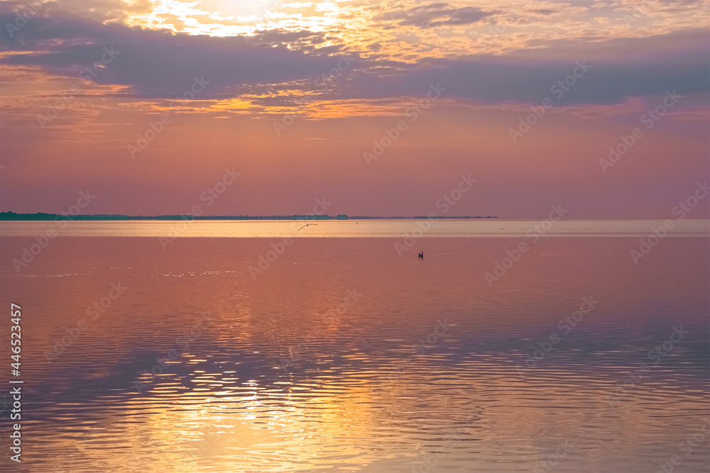 Amazing light at the morning on the sea. Colorful glowing peach clouds, soft light. Symmetry reflections on water, natural mirror, water surface texture. Idyllic seascape.
