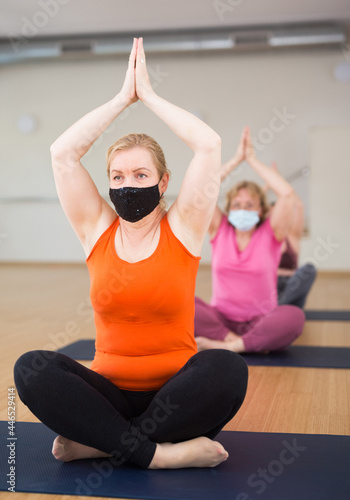 Mature woman in protective mask making yoga meditation in yoga pose - agni stambhasana