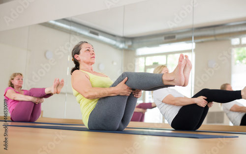 Portrait of mature active woman practicing group yoga, making balancing asana