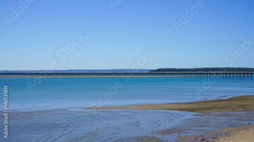 Panoramic view of Urangan Pier at low tide, with beach and blue water in the foreground and Fraser Island on the horizon. Hervey Bay, Queensland, Australia. 