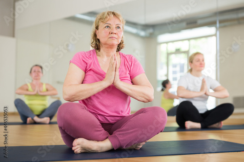 Aged European women are sitting in a half lotus pose in fitness room