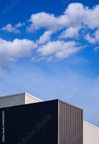 Low angle view of black and white corrugated metal factory buildings against clouds and blue sky background in vertical frame 
