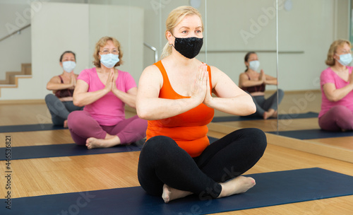 Active senior woman practicing group yoga, sitting in lotus posture and meditating