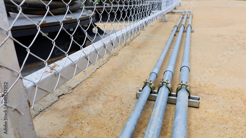 Metal pipe clamp on concrete floor. Outdoor electrical wiring technology to prevent possible damage to cables on the side of the grate fence. Turn off focus and select an object. photo