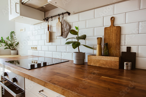 Kitchen brass utensils, chef accessories. Hanging kitchen with white tiles wall and wood tabletop.Green plant on kitchen background photo