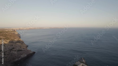 Drone flying out from cliffside chapel from fort of Santo António de Belixe toward the endless Atlantic ocean.