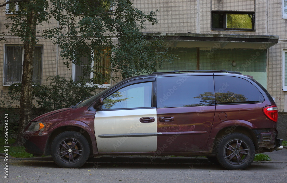 An old dark red automobile with a silver door in the courtyard of a residential building, Bolshevikov Avenue, St. Petersburg, Russia, July 2021