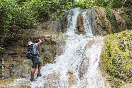 Young man exploring and taking photos of waterfall in mountain during vacations.