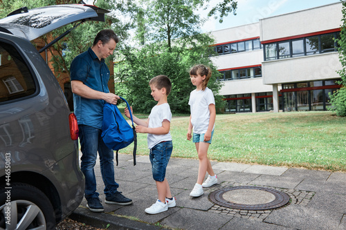 Dad, father sees off, leads the children to school, brother and sister, boy and girl, takes backpacks out of the car. School days, the beginning of the school day