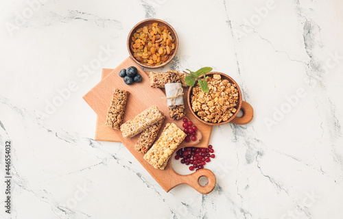 Board with healthy cereal bars and berries on light background