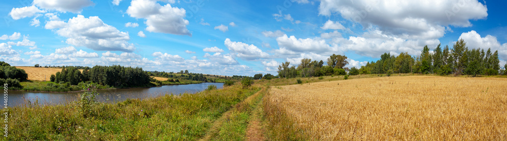 Summertime scenery.Beautiful rural view of blue sky over the calm river and golden wheat fields during sunny summer day.Summer countryside panorama.