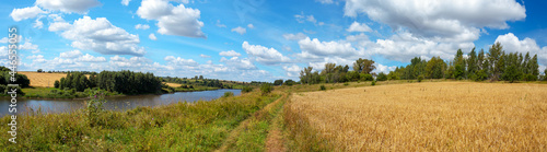 Summertime scenery.Beautiful rural view of blue sky over the calm river and golden wheat fields during sunny summer day.Summer countryside panorama.