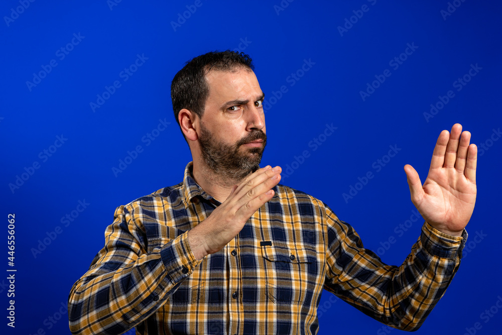 Naklejka premium Attractive and serious adult man with mustache shows karate chop gesture isolated on blue background