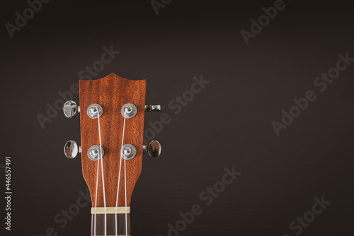 Only the head of the ukulele is brown oak on a black patterned table. Guitar Ukulele is a musical instrument that brings joy, entertainment, and is easy to carry anywhere