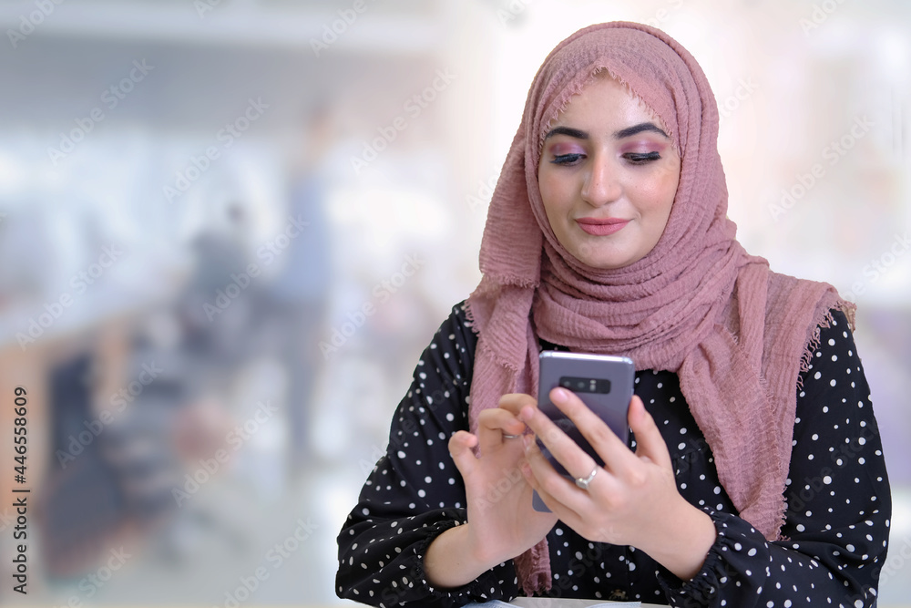 Female Arab at office using mobile phone at work duty wearing Hijab Abaya in the Middle East. Arabic business woman concept. Arab women on duty checking message. 