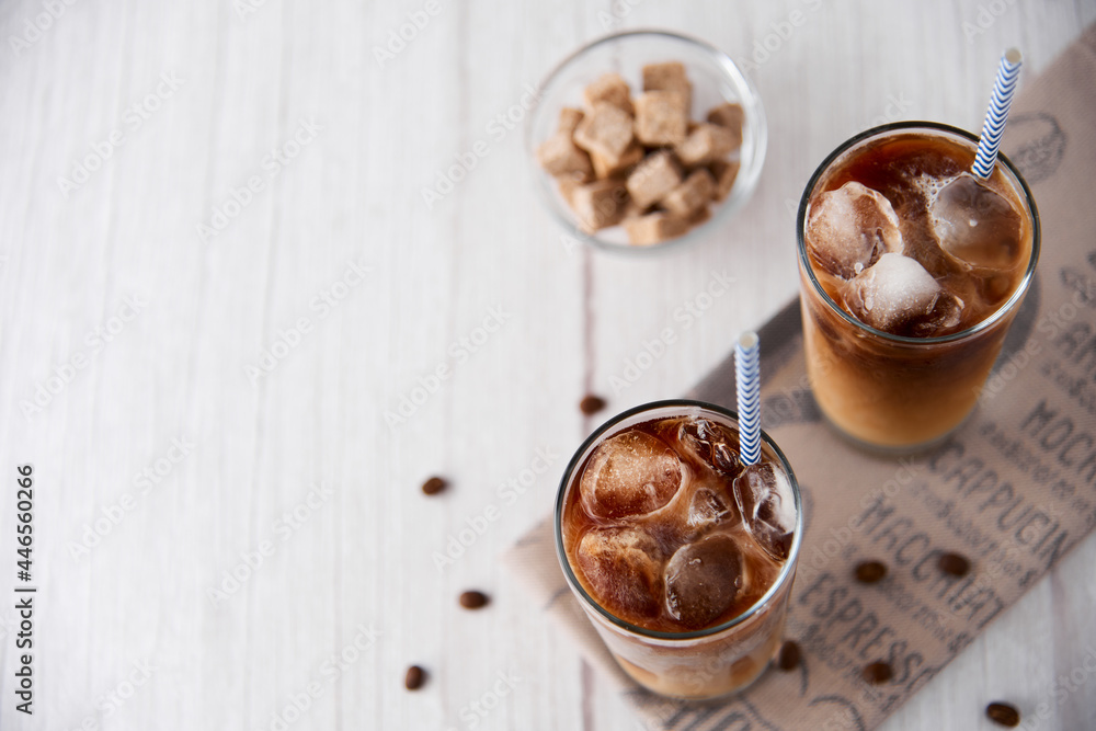 Iced coffee in a tall glass with cream or milk and beans, straws on light background. Cold tasty summer refreshment beverage concept. Selective focus, copyspace. Flat lay, top view. Iced coffee in a tall glass with cream or milk and beans, straws on light background. Cold tasty summer refreshment beverage concept. Selective focus, copyspace. Flat lay, top view.