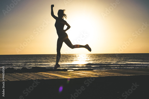 silhouette of a successful  strong  and sportive female doing champion pose with fists on beach boardwalk during sunset or sunrise  