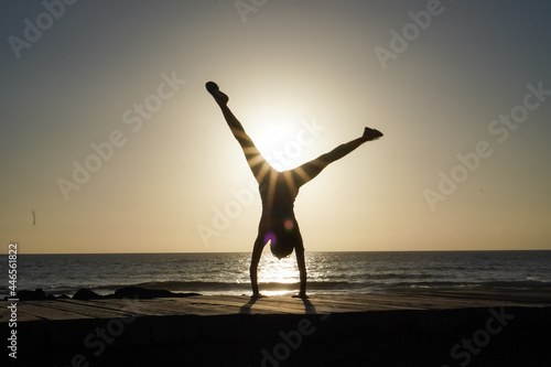 Obraz na plátne silhouette of a sportive athletic woman doing cartwheel on beach boardwalk durin