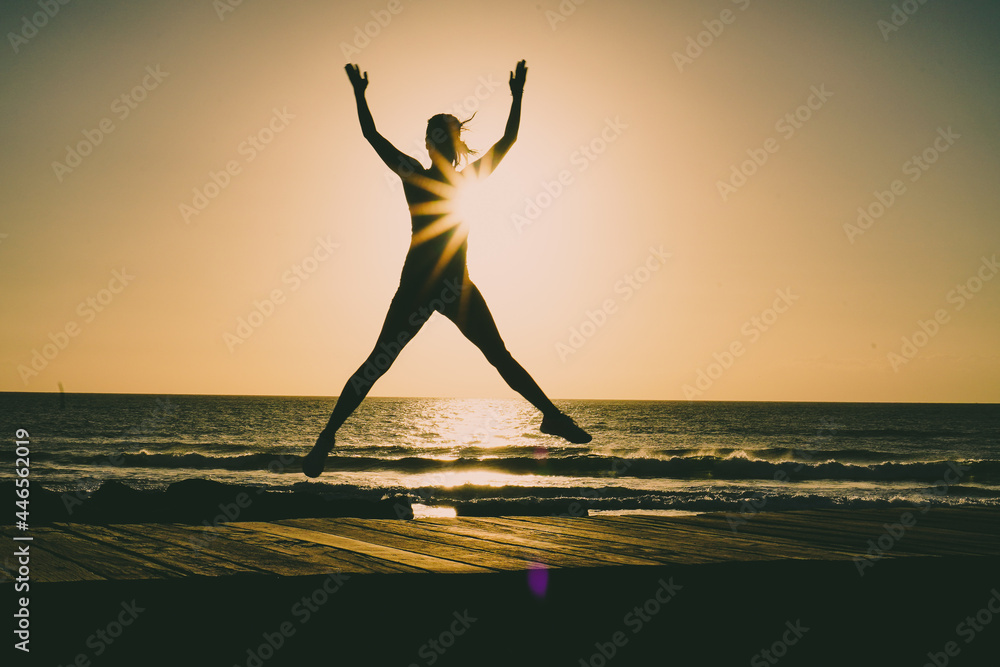 silhouette of a successful  jumping and  joyful woman on beach boardwalk during sunset or sunrise for motivation
