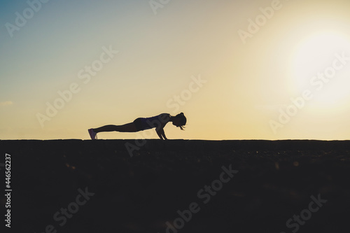 Fototapeta Naklejka Na Ścianę i Meble -  silhouette of a sportive athletic woman doing yoga on beach boardwalk during sunset 
