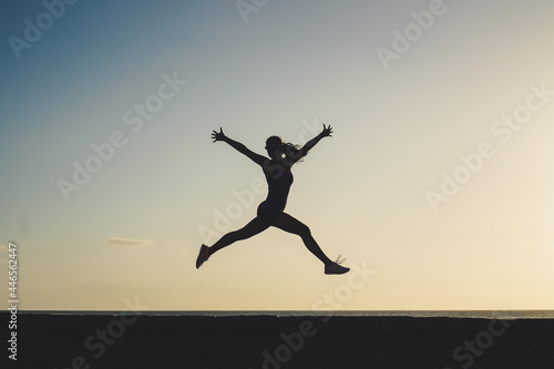 silhouette of a successful jumping and joyful woman on beach boardwalk during sunset or sunrise for motivation