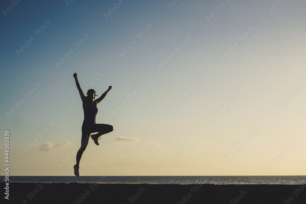 silhouette of a successful  jumping and  joyful woman on beach boardwalk during sunset or sunrise for motivation