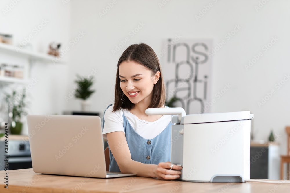 Young woman with deep fryer using laptop in kitchen Young woman with deep fryer using laptop in kitchen