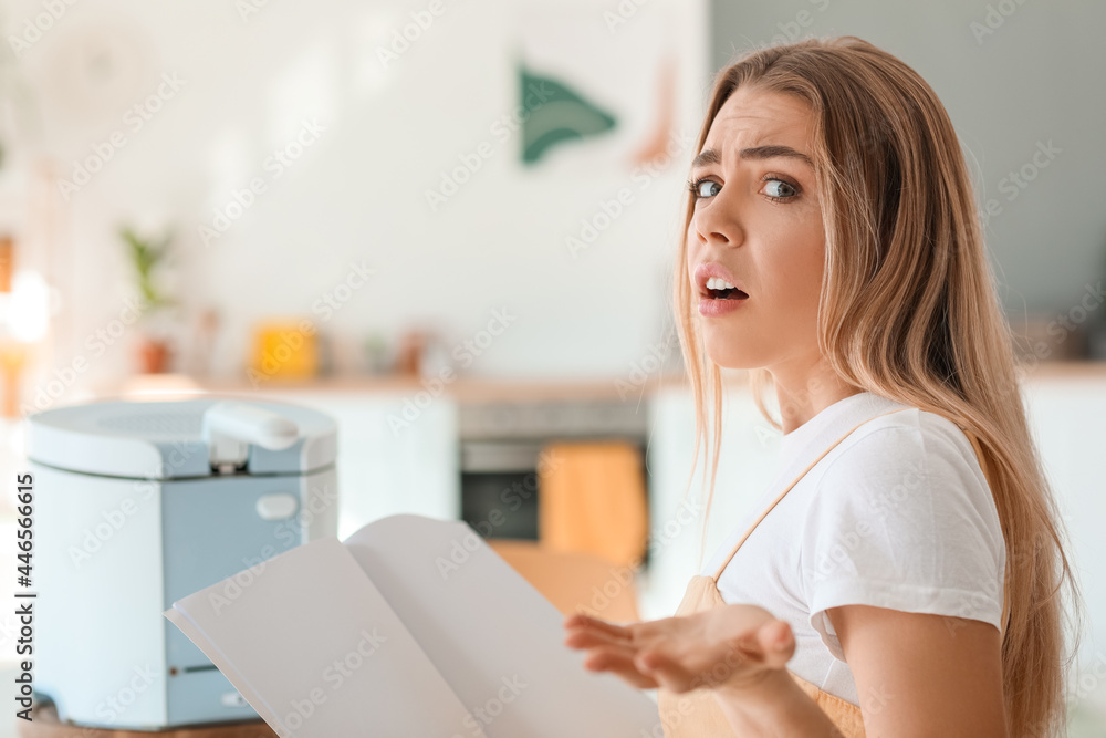 Upset young woman reading instruction book of deep fryer in kitchen Upset young woman reading instruction book of deep fryer in kitchen