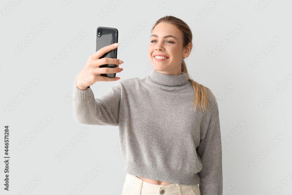 Young woman taking selfie on light background Young woman taking selfie on light background