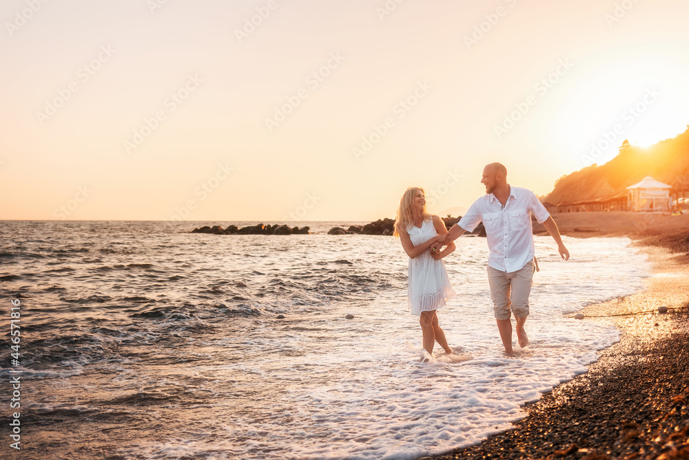 Just married. A happy young man and woman are having fun walking along the seashore. In the background, the sunset and the sky. Copy space. Concept of honeymoon