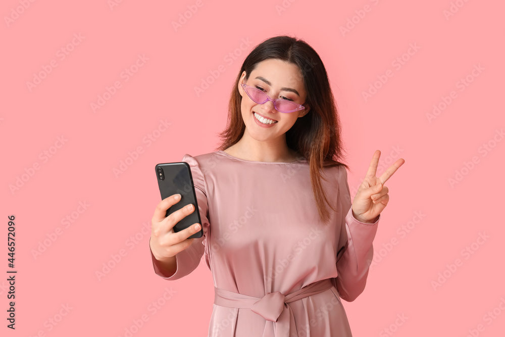 Stylish young Asian woman taking selfie on color background Stylish young Asian woman taking selfie on color background