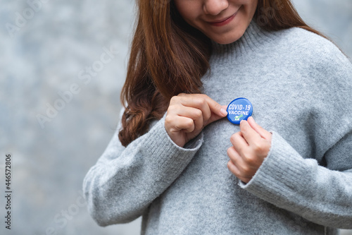 Foto Closeup image of a young woman putting Covid-19 vaccinated sign brooch on shirt