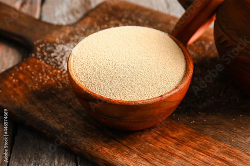 Bowl with active dry yeast on wooden background