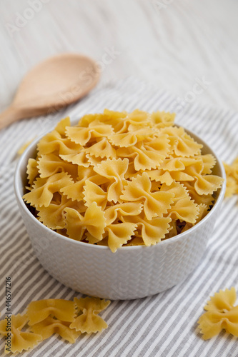 Dry Organic Farfalle Pasta in a Bowl on a white wooden background, low angle view.