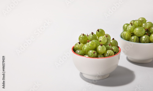 Bowls with fresh ripe gooseberry on light background