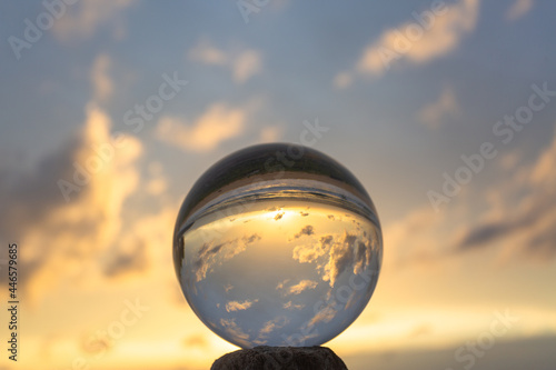 Fototapeta Naklejka Na Ścianę i Meble -  beautiful cloud and golden sunset inside crystal ball placed on a timber beside the beach..beautiful nature in a crystal ball by the sea..Unique and creative travel and nature idea..