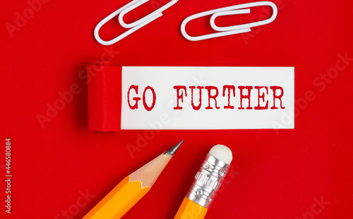 GO FURTHER message written under torn red paper with pencils and clips, business photo