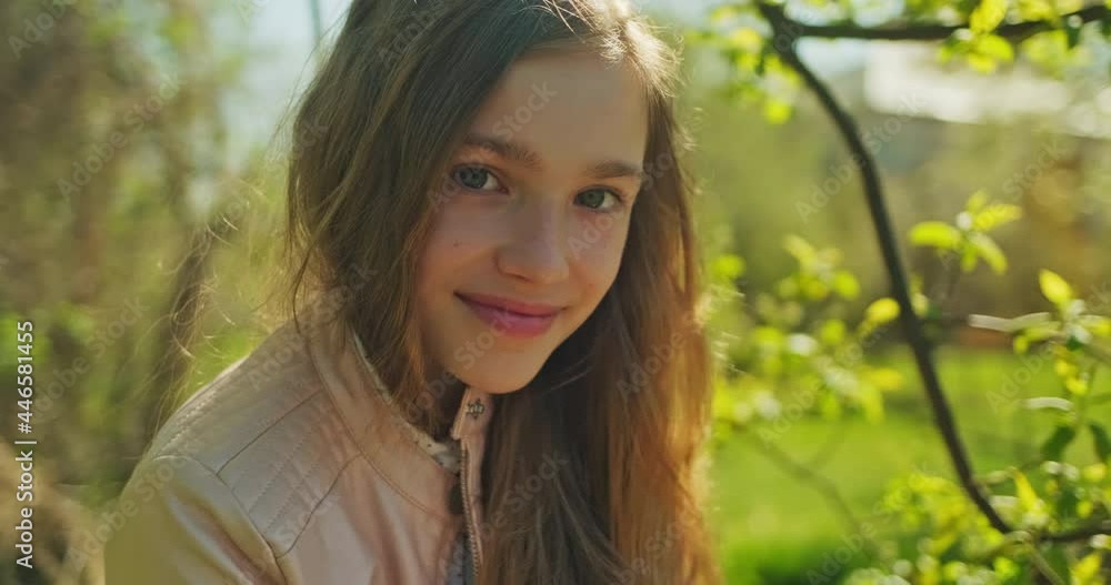 Preteen girl 10s has long blond hair, using mobile phone in the park and smiling at camera. Closeup portrait Preteen girl 10s has long blond hair, using mobile phone in the park and smiling at camera. Closeup portrait