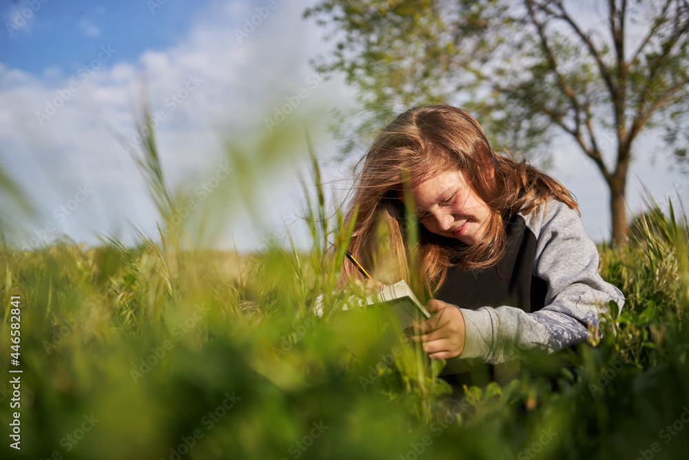 Cheerful girl drawing in notebook in field Cheerful girl drawing in notebook in field