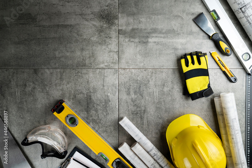 Contractor theme. Plans, tool kit of the contractor, yellow hardhat and libella. Gray tiles background. © zolnierek