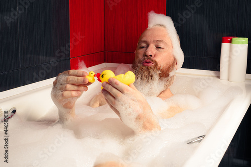 Obraz na płótnie Cute funny bearded man playing with rubber ducks in bubble bath relaxing at home w salonie