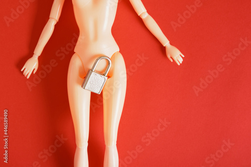 nude doll on a red background, metal lock between the doll's legs, padlock on the hips, sex education concept photo