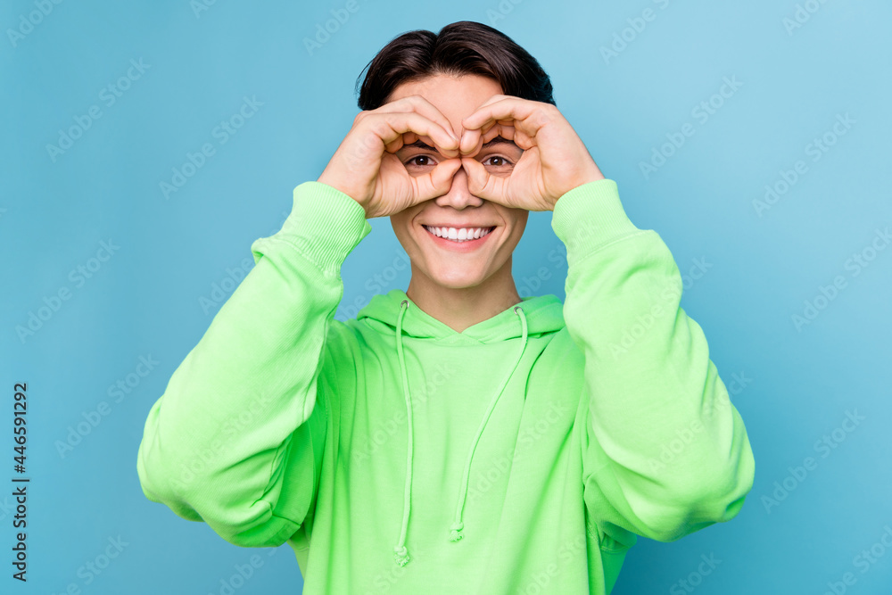 Photo of cute funny young guy dressed green hoodie showing fingers spectacles smiling isolated blue color background Photo of cute funny young guy dressed green hoodie showing fingers spectacles smiling isolated blue color background