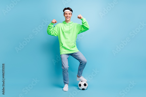 Fototapeta Naklejka Na Ścianę i Meble -  Photo of cool confident young guy dressed green hoodie playing football showing strength smiling isolated blue color background
