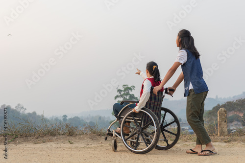 Disabled handicapped woman in wheelchair and care helper walking on trail at sunrise.