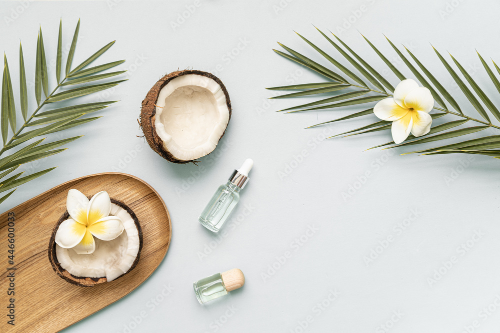 Coconut essential oil and palm leaf oil on a table with copy space on a pastel background. Styled composition of flat lay with tropical leaves and flowers. Coconut essential oil and palm leaf oil on a table with copy space on a pastel background. Styled composition of flat lay with tropical leaves and flowers.