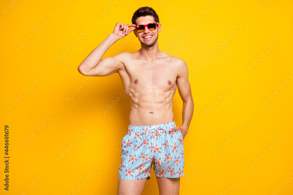 Portrait of attractive shirtless cheerful guy touching specs sea resort season isolated over bright yellow color background