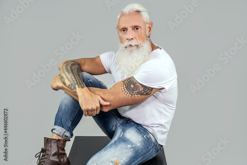 Fashionable senior man with white beard posing in studio, wearing white tshirt and jeans. photo